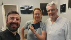 Unverfälschtes Selfie von drei Personen in einer Galerie, die Frau hält einen Abzug in der Hand; warme Beleuchtung, praktischer Einzelunterricht in der Fotografie in Berlin.