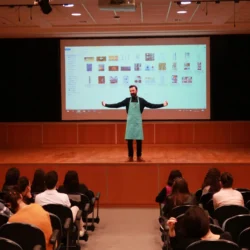 Ein Dozent in einer Schürze leitet einen praktischen Fotografie-Workshop mit projizierten Bildern und bezieht die sitzenden Schüler in Berlin mit ein.