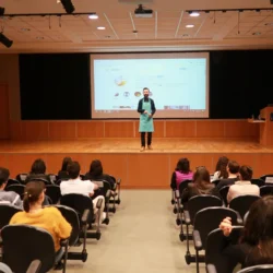 Ein Referent in Schürze leitet einen praktischen Fotografie-Workshop auf der Bühne vor sitzenden Studenten in einem gut beleuchteten Hörsaal in Berlin.