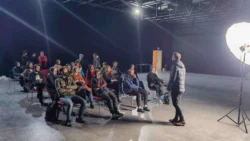 Ein Dozent leitet einen praktischen Fotografie-Workshop in einem Berliner Studio, die Teilnehmer sitzen unter dramatischer, weicher Dauerbeleuchtung.