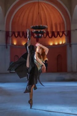 Tonozlu bir tiyatroda, sinematik sıcak arka ışık ve soğuk ön planda, orta uzanışta bir balerinin dinamik sanatçı portresi; fotoğrafçı Berlin'de.