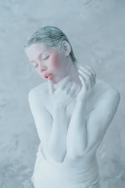 Porcelain-painted model in soft studio light, delicate pose against a textured backdrop — cinematic beauty photography in Europe.