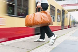 Berlin'de bir platformda ten rengi deri bir spor çantası taşıyan bir kişinin bulanık tramvay ile düşük açılı çekimi - Avrupa'da dinamik ürün fotoğrafçılığı.