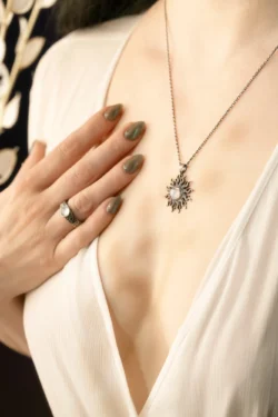 Modelin dekoltesindeki güneş kolyesinin manikürlü el ile yakın plan stüdyo çekimi, Berlin'de cilalı ürün fotoğrafçılığı.