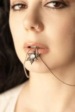 Cilalı güzellik fotoğrafçılığı: yumuşak sıcak ışıkta dudaklarının arasında yıldız kolye tutan bir kadının yakın çekimi, Avrupa için fotoğrafçı.