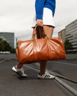 Berlin'de, bir modelin ten rengi deri bir spor çantasını şehrin sokaklarında taşıdığını gösteren, sinematik ışıklandırmalı, yerinde çekilmiş cilalı ürün fotoğrafçılığı.