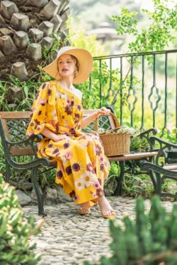 Güneşli bir bahçe bankında sarı çiçekli elbiseli ve geniş hasır şapkalı kadın, sinematik moda çekimi, Avrupa için fotoğrafçı