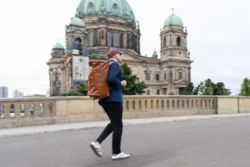 Berlin'de, deri sırt çantasıyla Berliner Dom'un önünden geçen bir adamın yerinde çekilmiş kişisel marka fotoğrafı, dinamik hareket.