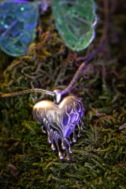 Berlin'de, mor ışıklı, yosun üzerinde eriyen damlalara sahip yontulmuş gümüş kalp kolyenin cilalı ürün fotoğrafı yakın çekimi.