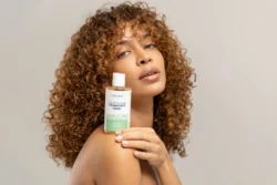 Omzunda cilt bakım toniği tutan kıvırcık saçlı bir modelin cilalı stüdyo güzellik portresi - Berlin'de güzellik ve ürün fotoğrafçılığı.