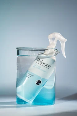 Avrupa'daki projeler için mavi sıvı dolu bir beher içinde buzlu Relance 2-Fazlı Saç Kremi sprey şişesinin cilalı stüdyo ürün fotoğrafı.