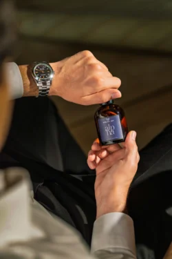 Sıcak ışıkta saatli kehribar parfüm şişesini tutan ellerin cilalı ürün çekimi - Avrupa genelinde ürün fotoğrafçılığı.