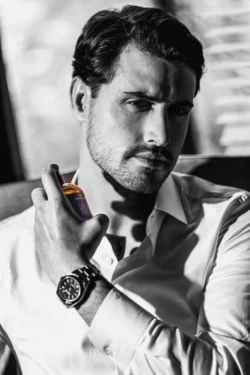 Parfüm şişesi tutan bir erkek modelin karamsar siyah-beyaz portresi, Avrupa'daki projeler için sinematik reklam fotoğrafçılığı.