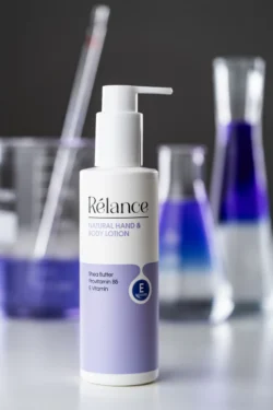 Beyaz ve leylak renkli Rélance el ve vücut losyonunun stüdyoda çekilmiş cilalı ürün fotoğrafı ve bulanık laboratuvar cam malzemeleri, fotoğrafçı Berlin.