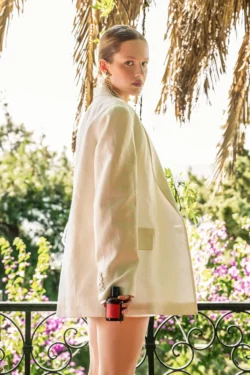 Parfüm şişesi tutan beyaz blazer ceketli bir modelin arkadan aydınlatmalı sinematik portresi - Avrupa'daki projeler için güzellik fotoğrafçılığı.