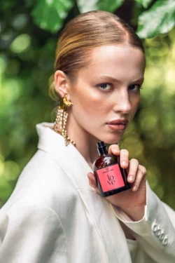 Love parfüm şişesi tutan bir modelin yeşil bokeh'e karşı yakın plan portresi, Avrupa'da gösterişli güzellik ürünleri fotoğrafçılığı