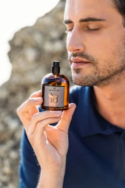 Güneşin aydınlattığı kıyı kayalığına karşı amber parfüm şişesini içine çeken adam, Avrupa'daki projeler için cilalı ürün fotoğrafçılığı.