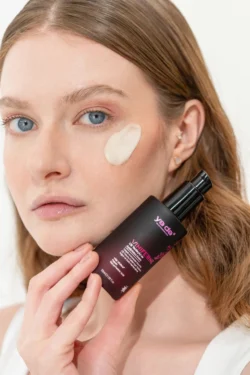 Yanağında mat siyah bir şişe tutan kremli bir modelin yakın çekimi - Avrupa için bir fotoğrafçı tarafından cilalanmış güzellik ürünü fotoğrafçılığı.