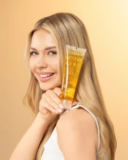 Berlin'de yaşayan bir fotoğrafçı tarafından Avrupa'daki projeler için çekilen, elinde altın bir şampuan tüpü tutan gülümseyen bir modelin cilalı stüdyo ürün fotoğrafı.