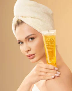 Havluyla sarılmış saçlarıyla altın bir şampuan tüpü tutan bir modelin cilalı stüdyo güzellik çekimi - Avrupa'daki müşteriler için güzellik fotoğrafçılığı.