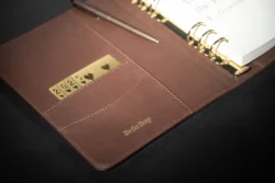 Altın halkalı ve BeSo Busy kabartmalı deri ajandanın yumuşak ışıkla aydınlatılmış cilalı ürün fotoğrafı - Avrupa için fotoğrafçı.