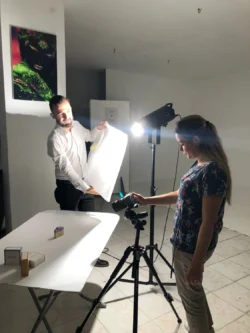 Ein Fotograf unterrichtet einen Studenten in einem praktischen privaten Fotografiekurs in Berlin und demonstriert ihm die Studiobeleuchtung und den Produktaufbau.