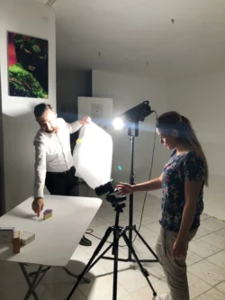Der Dozent leitet einen Studenten bei einer praktischen Produktaufnahme an, bei der Licht und Komposition angepasst werden; privater Fotografieunterricht in Berlin.