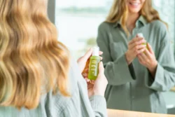 Avrupa'daki projeler için ayna cilalı güzellik ve ürün fotoğrafçılığında yeşil bir cilt bakım şişesi tutan bir kadının yumuşak ışıklı portresi.