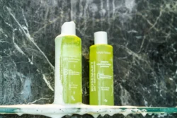 Cam rafta koyu mermer üzerinde köpüklü iki kireç yeşili şampuan şişesinin cilalı ürün fotoğrafı, Avrupa'daki projeler için fotoğrafçı.