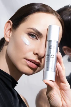 Gümüş havyar kremi şişesini tutan yanağında krem olan modelin yakın çekimi, parlak stüdyo aydınlatması, Avrupa için ürün fotoğrafçılığı.