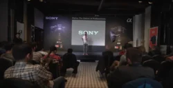 Referent auf der Bühne mit SONY-Projektion, Kamerabannern und Softbox, während ein sitzendes Publikum zuhört - praxisnahes Fotoseminar in Berlin.