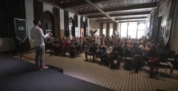 Referent auf der Bühne spricht vor einem Hörsaal in einem historischen Gebäude, filmische Stimmung bei wenig Licht - Fotoseminar, Praxistraining in Berlin.